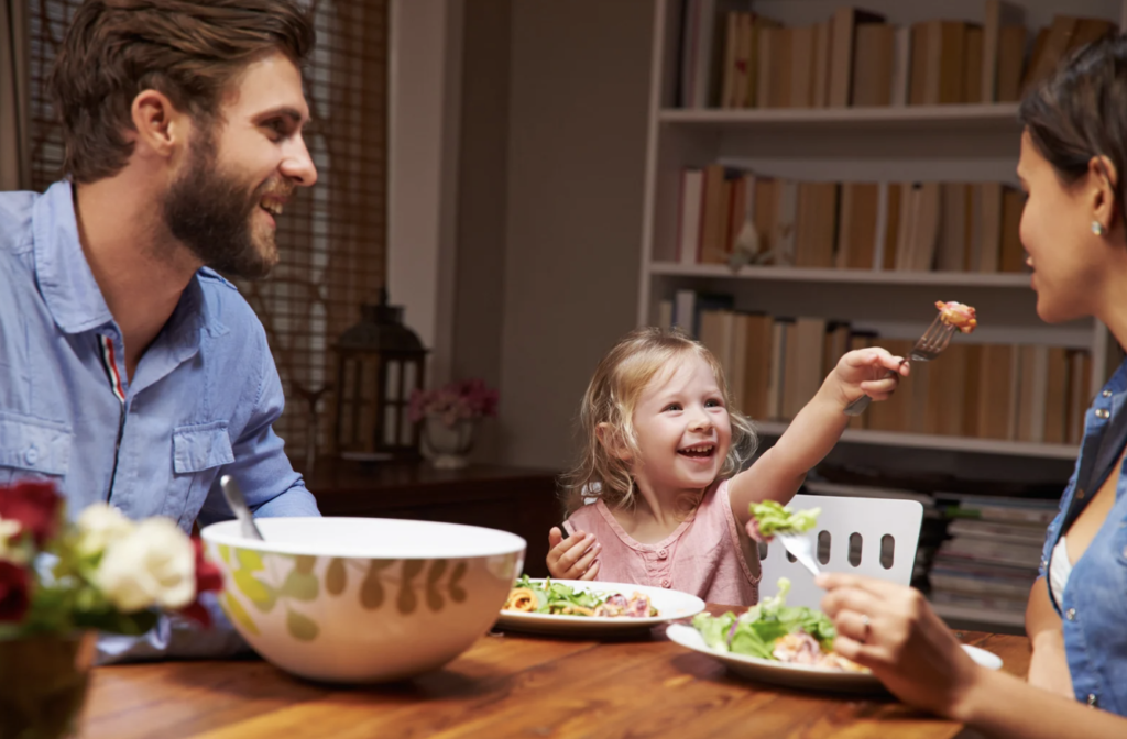 Parent and child sitting together at a kitchen table, exploring a variety of foods in a relaxed and supportive environment.